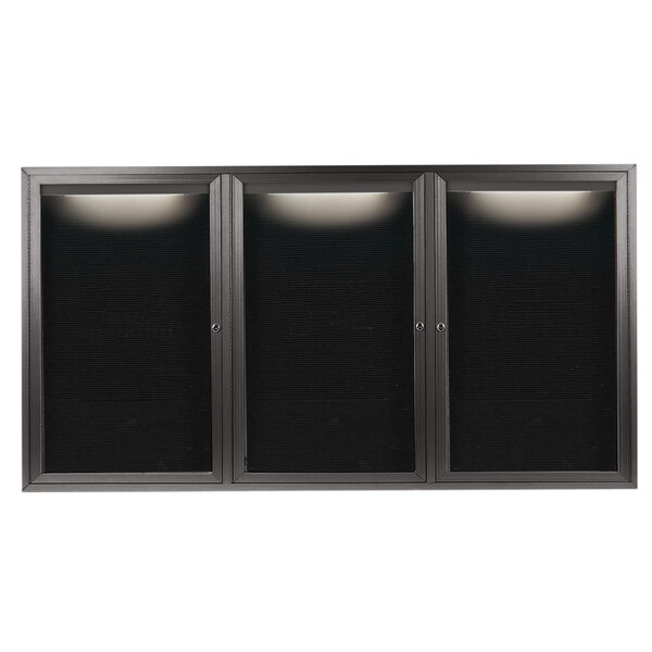 A black rectangular cabinet with three bronze metal doors with a black letter board inside.