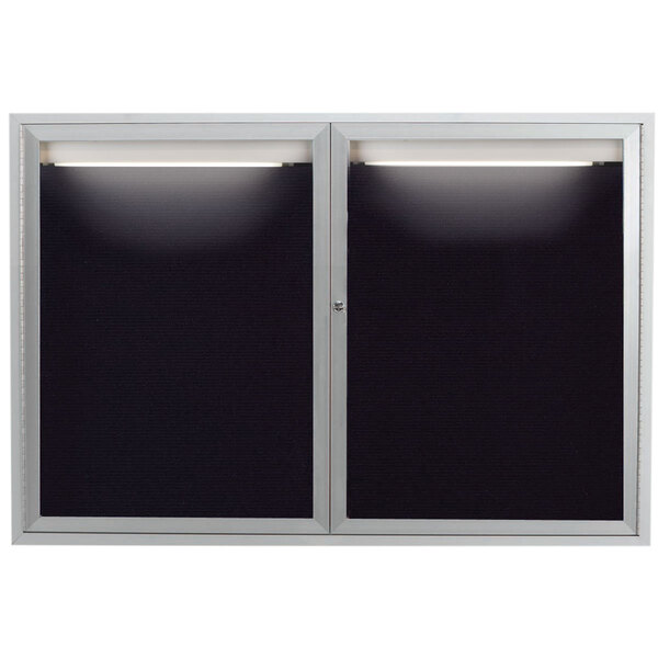 A black and silver framed Aarco message center with two glass doors and lights on the inside.
