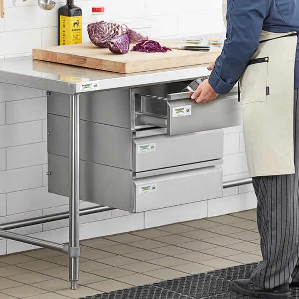 A person in a white apron opening a Regency stainless steel drawer in a professional kitchen counter.