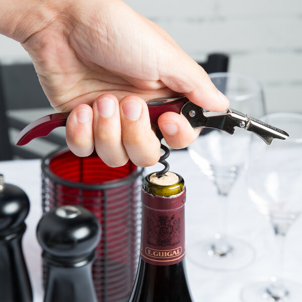 A hand holding a Pulltap's Original burgundy waiter's corkscrew and opening a wine bottle.