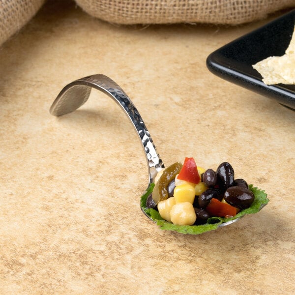 A Bon Chef Reflections bouillon tasting spoon filled with food on a table.