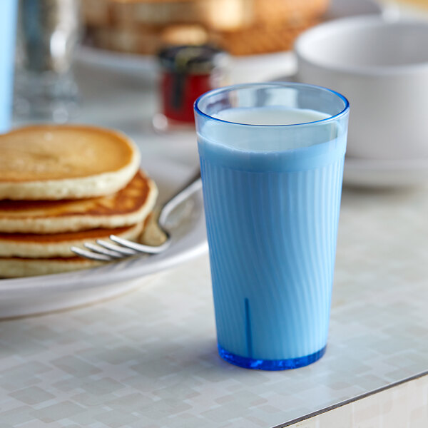 A blue Thunder Group Belize plastic tumbler filled with milk on a table with a stack of pancakes and a fork.