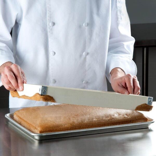 A chef using a MFG Tray fiberglass sheet pan extender to cut a large piece of cake.