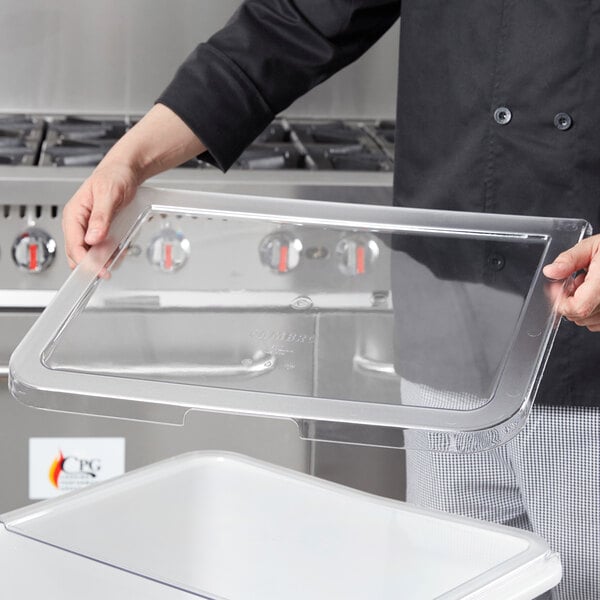 A person holding a clear plastic container and a white Cambro lid on a clear tray.