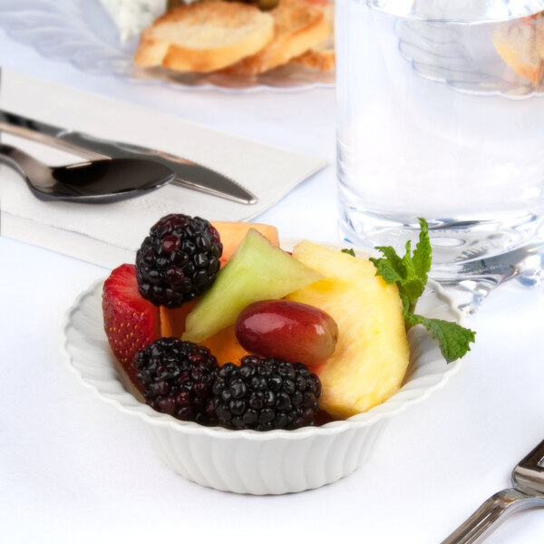A white Fineline plastic bowl filled with fruit on a table.