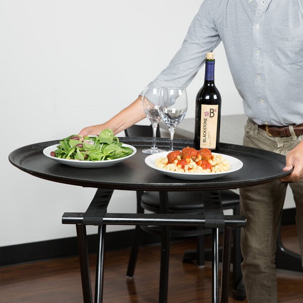 A man standing with a Carlisle non-skid oval serving tray holding a plate of pasta and meatballs and a glass of wine.
