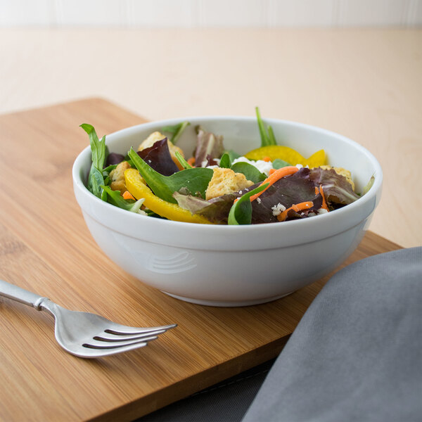 A Libbey alpine white porcelain nappie bowl filled with salad on a wooden table.