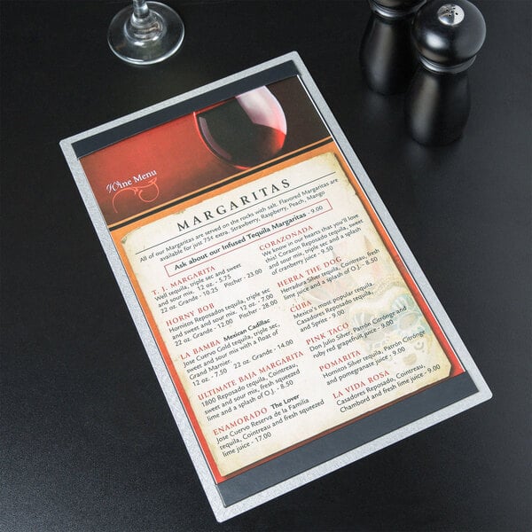 A Menu Solutions Alumitique aluminum menu board on a table with a wine glass and a menu.