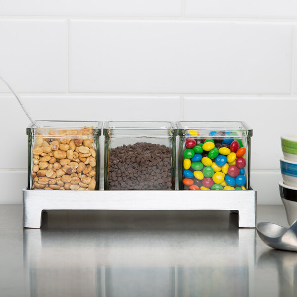 A Cal-Mil aluminum display with three glass jars filled with different candies and peanuts.
