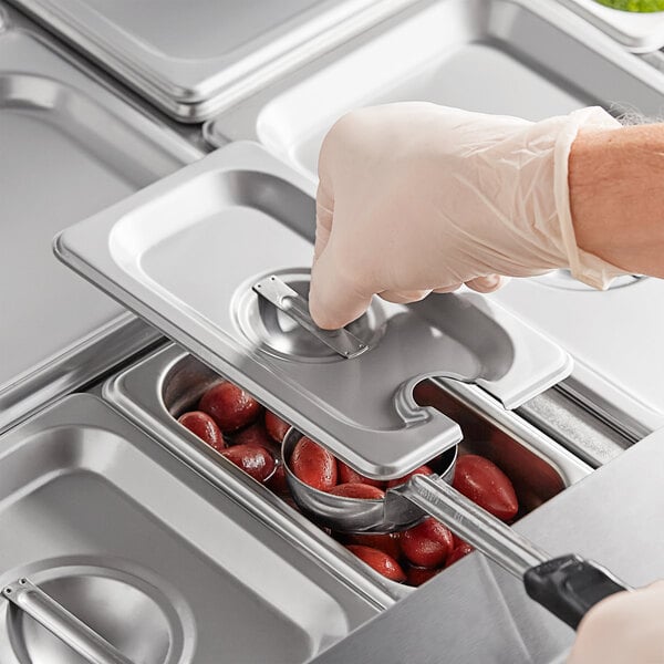 A hand in a white glove using a stainless steel slotted steam table pan cover to put food into a tray.