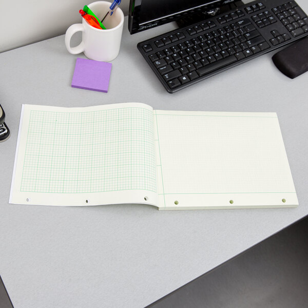 A notebook with green graph paper on a desk with pens and a keyboard.