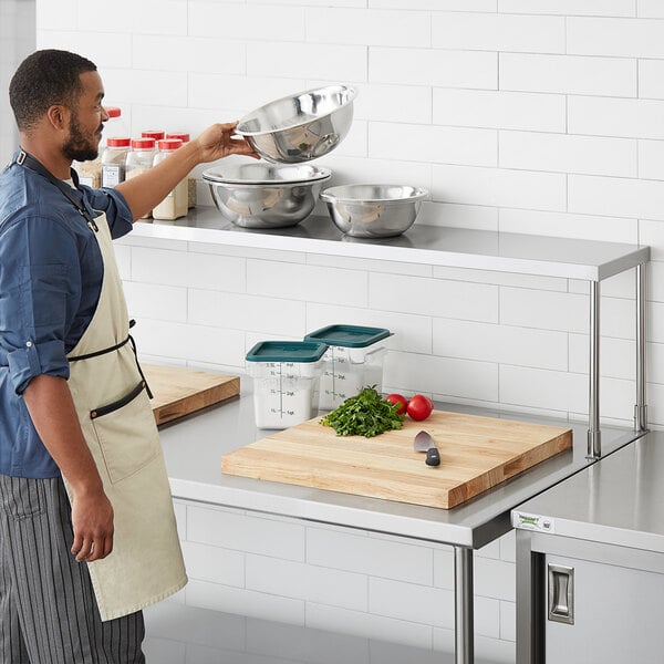 A man in an apron using a Regency stainless steel table mounted overshelf in a professional kitchen.