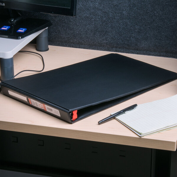 A Cardinal black binder with a red locking tab on a black surface.