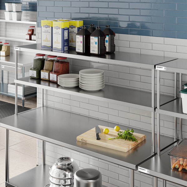 A stainless steel double deck overshelf with various kitchen items including spices, plates, bottles, and a cutting board with a knife and vegetables.