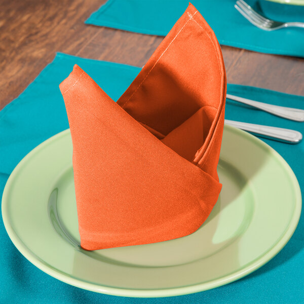 An orange Intedge cloth napkin folded on a plate.