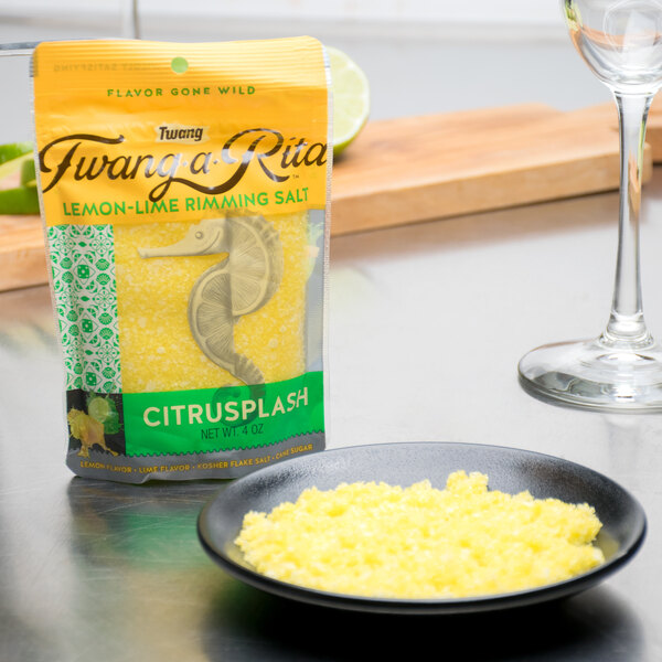 A bag of Twang-a-Rita Citrusplash Lemon-Lime Rimming Salt next to a glass of yellow liquid.