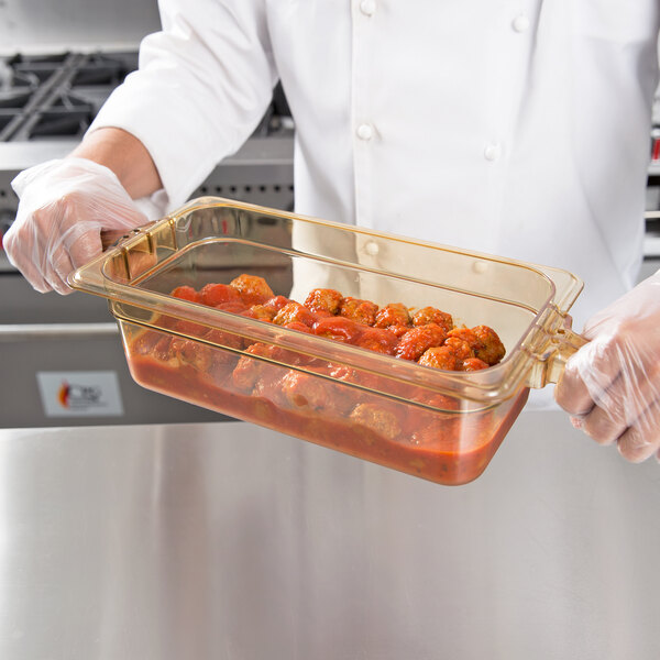 A person holding a Carlisle amber plastic food pan with food.