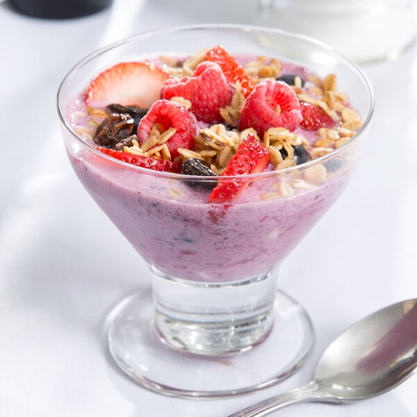 A Libbey dessert glass filled with fruit and oatmeal with a spoon in it.