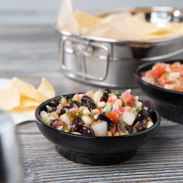 A black Thunder Group melamine salsa dish filled with salsa on a table next to a bowl of black beans.
