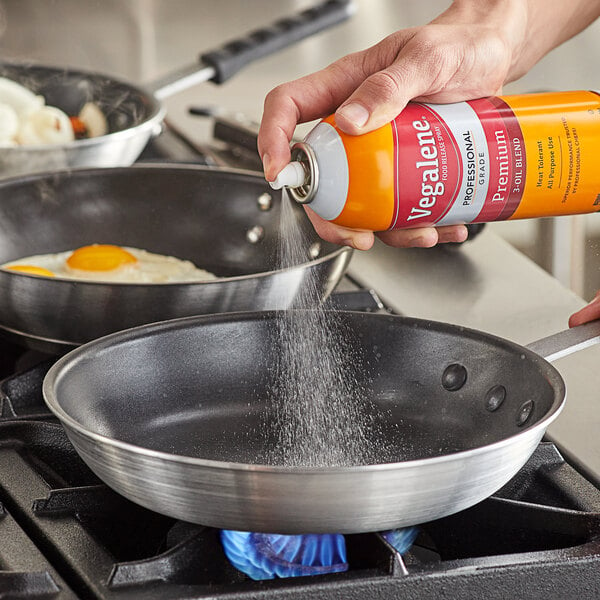 A hand using Vegalene All Purpose Release Spray on a pan with food in it.