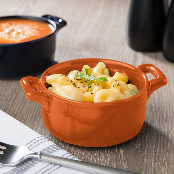 An orange porcelain bowl of macaroni and cheese on a table.