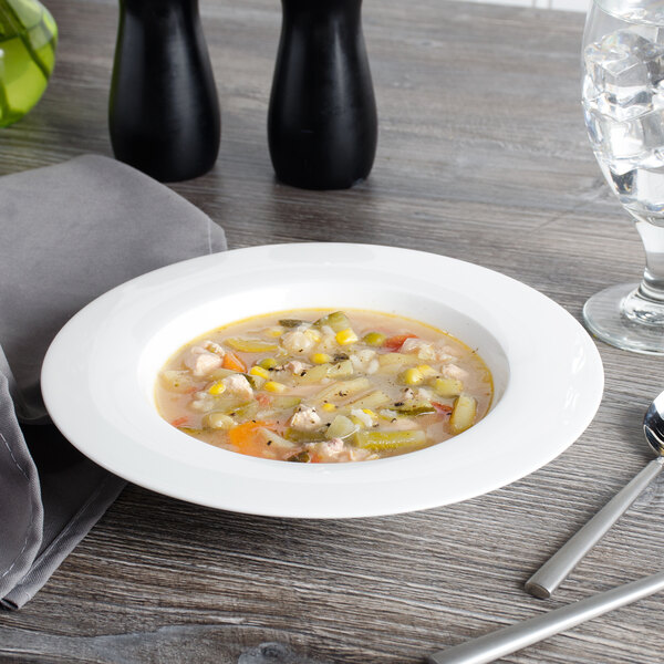 A wide rim white bone china bowl of soup with a spoon on a table.