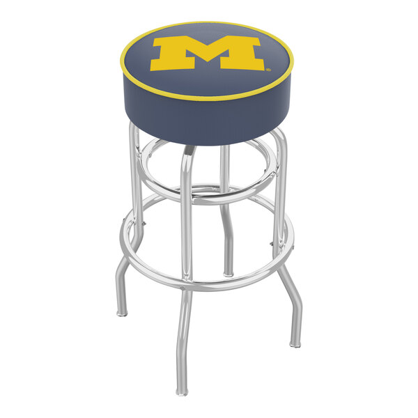 A Holland Bar Stool University of Michigan swivel bar stool with a blue and yellow logo on the seat.