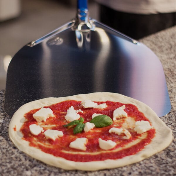 An Azzurra square pizza with cheese and basil on a counter being lifted with a GI Metal square pizza peel.