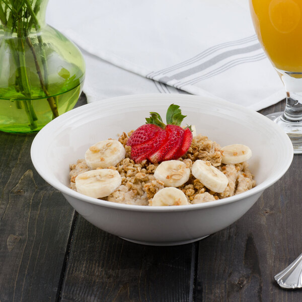 A white porcelain bowl filled with oatmeal topped with bananas and strawberries.