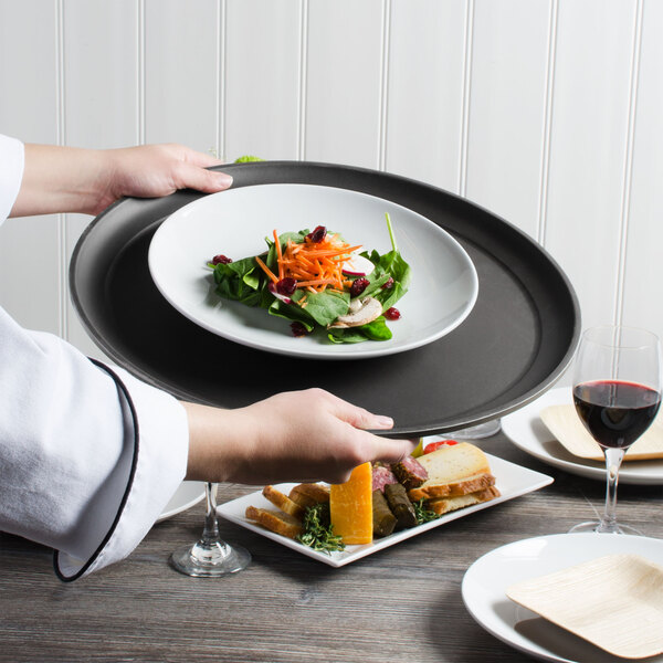 A person holding a Cambro black non-skid serving tray with a plate of salad and a glass of red wine.