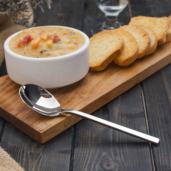 A bowl of soup on a wooden board with a Walco stainless steel bouillon spoon.