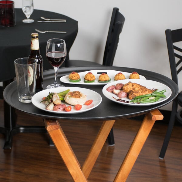 A black Cambro non-skid oval serving tray with food and wine on a table.