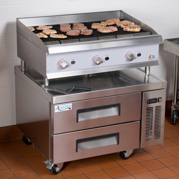 A Cooking Performance Group gas charbroiler on a stainless steel chef station counter with meat cooking on it.