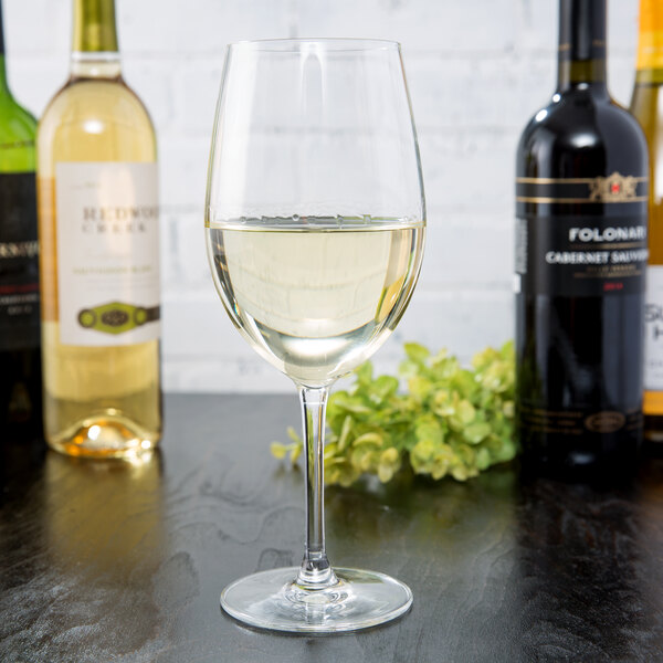 A Reserve by Libbey wine glass filled with white wine on a table with bottles of wine.