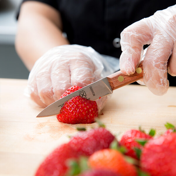 A person using a Mercer Praxis paring knife with a rosewood handle to cut a strawberry.