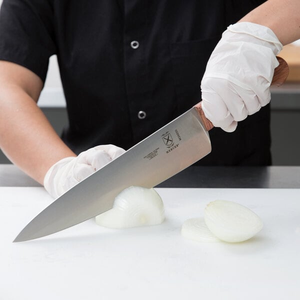 A person in gloves using a Mercer Culinary Praxis chef's knife to slice a white onion.