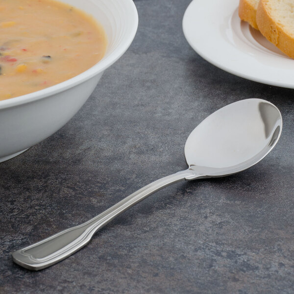 A Walco Luxor stainless steel bouillon spoon in a bowl of soup on a table.