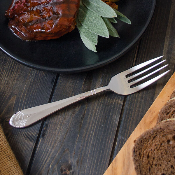 A Walco stainless steel table fork next to a plate of meat and bread.
