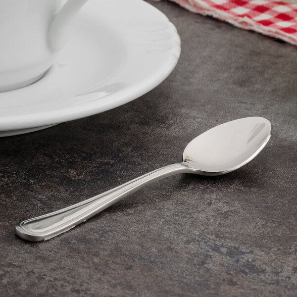 A Walco Pacific Rim stainless steel demitasse spoon on a table next to a cup.