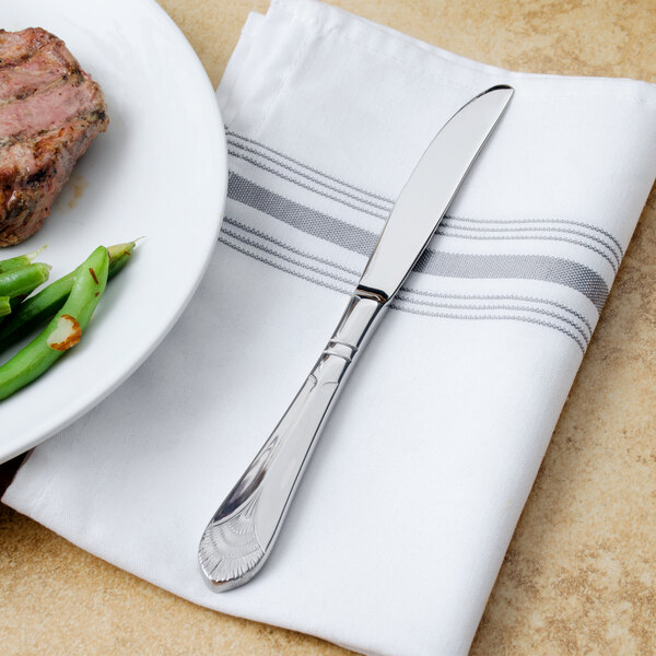 A Walco stainless steel dinner knife on a white napkin next to a plate of steak and green beans.