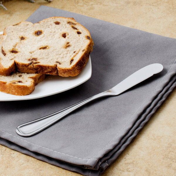 A Walco stainless steel butter knife on a plate with a piece of bread.