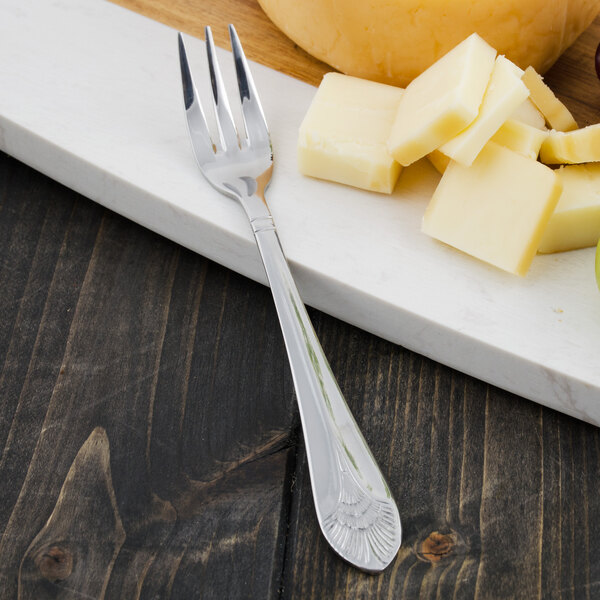 A Walco stainless steel cocktail fork next to cheese and fruit on a cutting board.