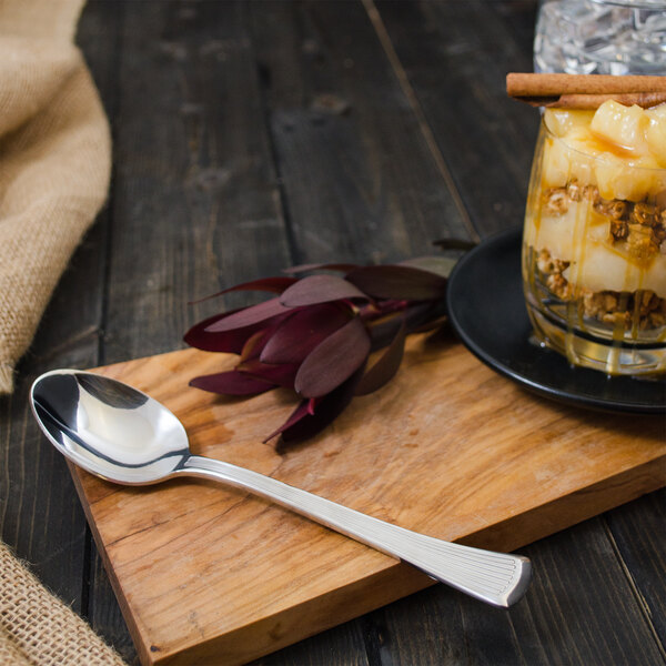 A Walco Bosa Nova stainless steel dessert spoon with a glass of fruit dessert on a wood board.
