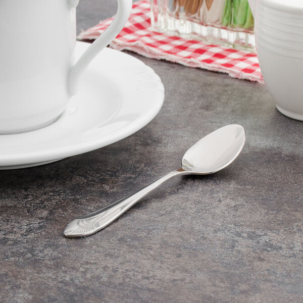 A Walco stainless steel demitasse spoon on a table next to a white cup.