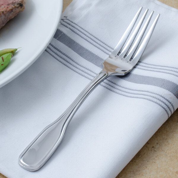 A Walco Saville stainless steel dinner fork on a napkin next to a plate with a piece of meat.