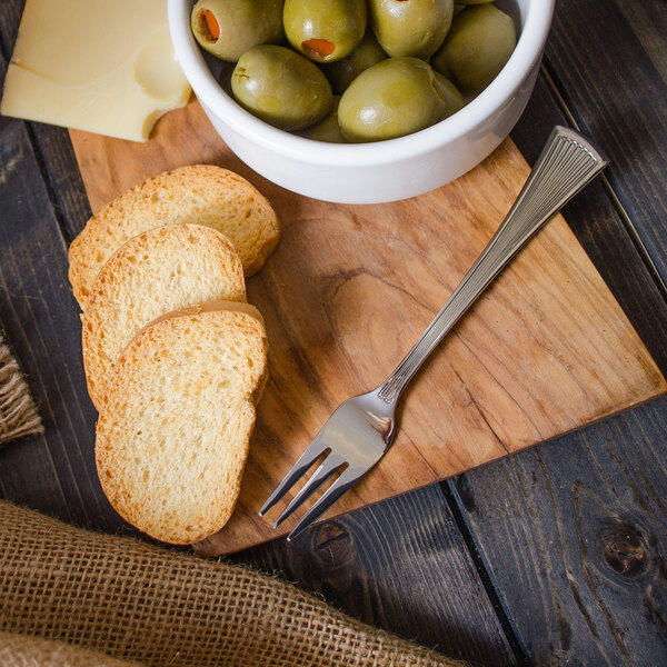 A bowl of olives and a Walco Bosa Nova cocktail fork on a wood board.
