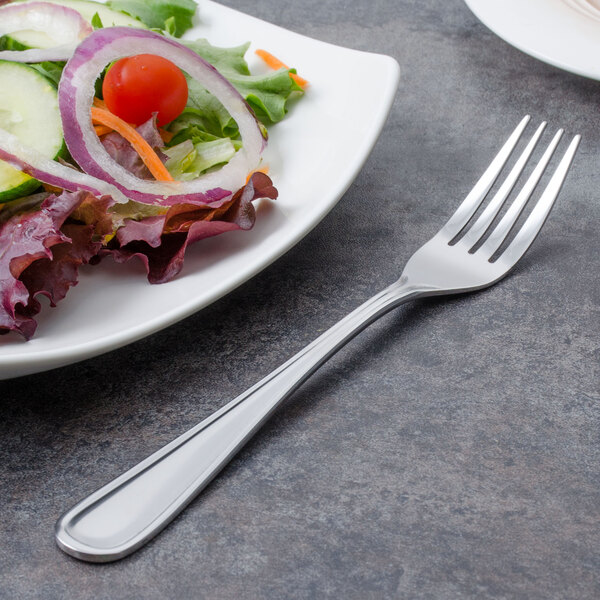 A Walco stainless steel utility fork next to a plate of salad.