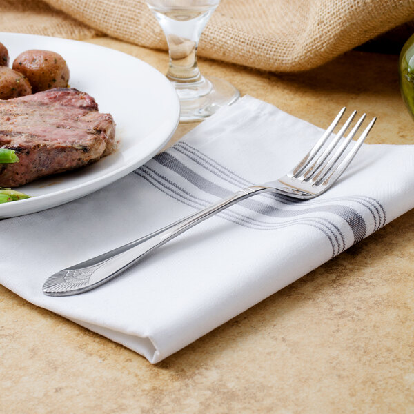 A Walco Meteor stainless steel table fork on a plate of steak and potatoes with a knife.