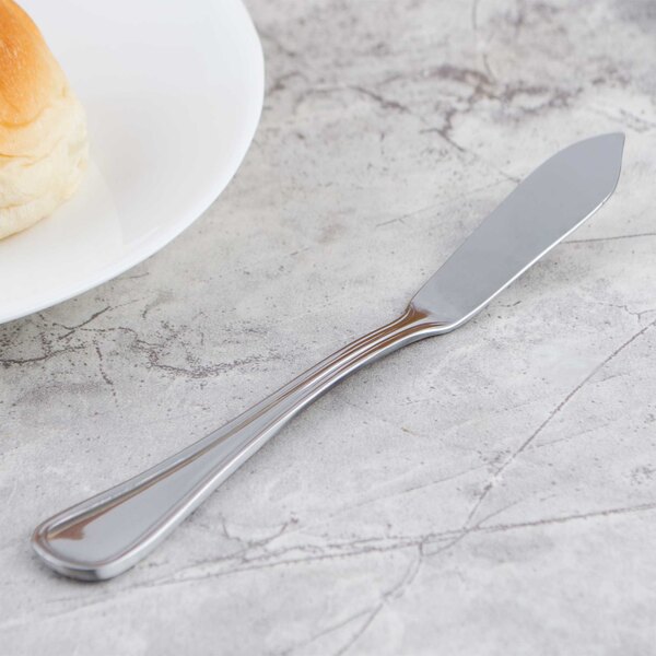 A Walco Marcie stainless steel butter spreader on a table with bread and butter.