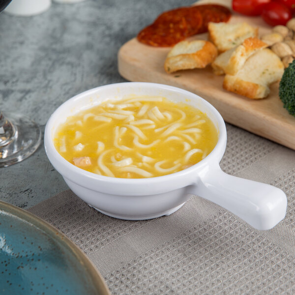 A white Melamine soup bowl with a handle filled with soup and noodles.